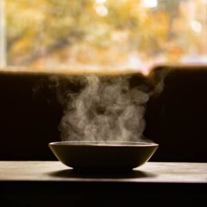 A steaming bowl of soup on a wooden table indoors with soft autumn light through a window.